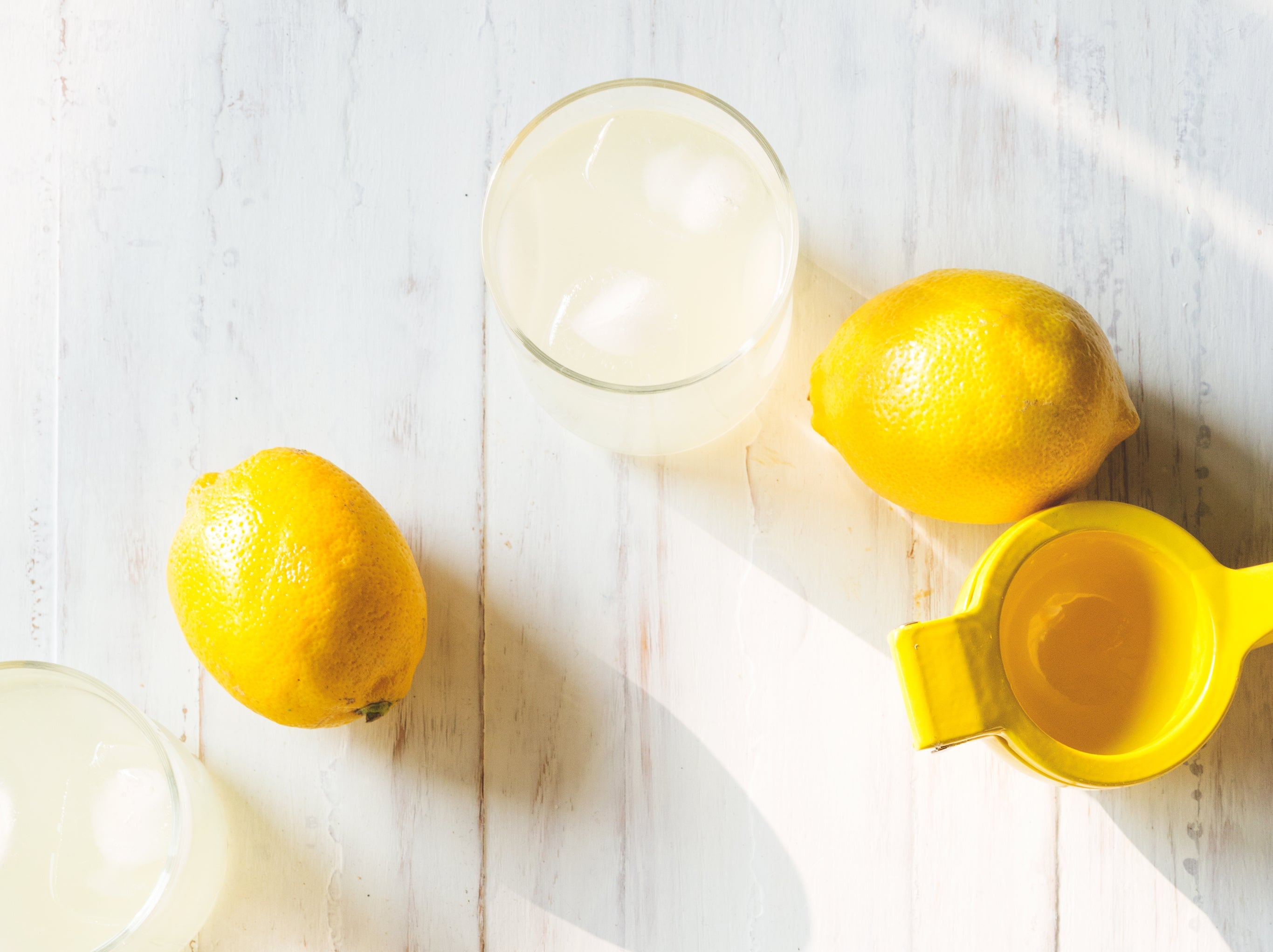 Fresh lemons and a glass of lemon water on a white wooden table