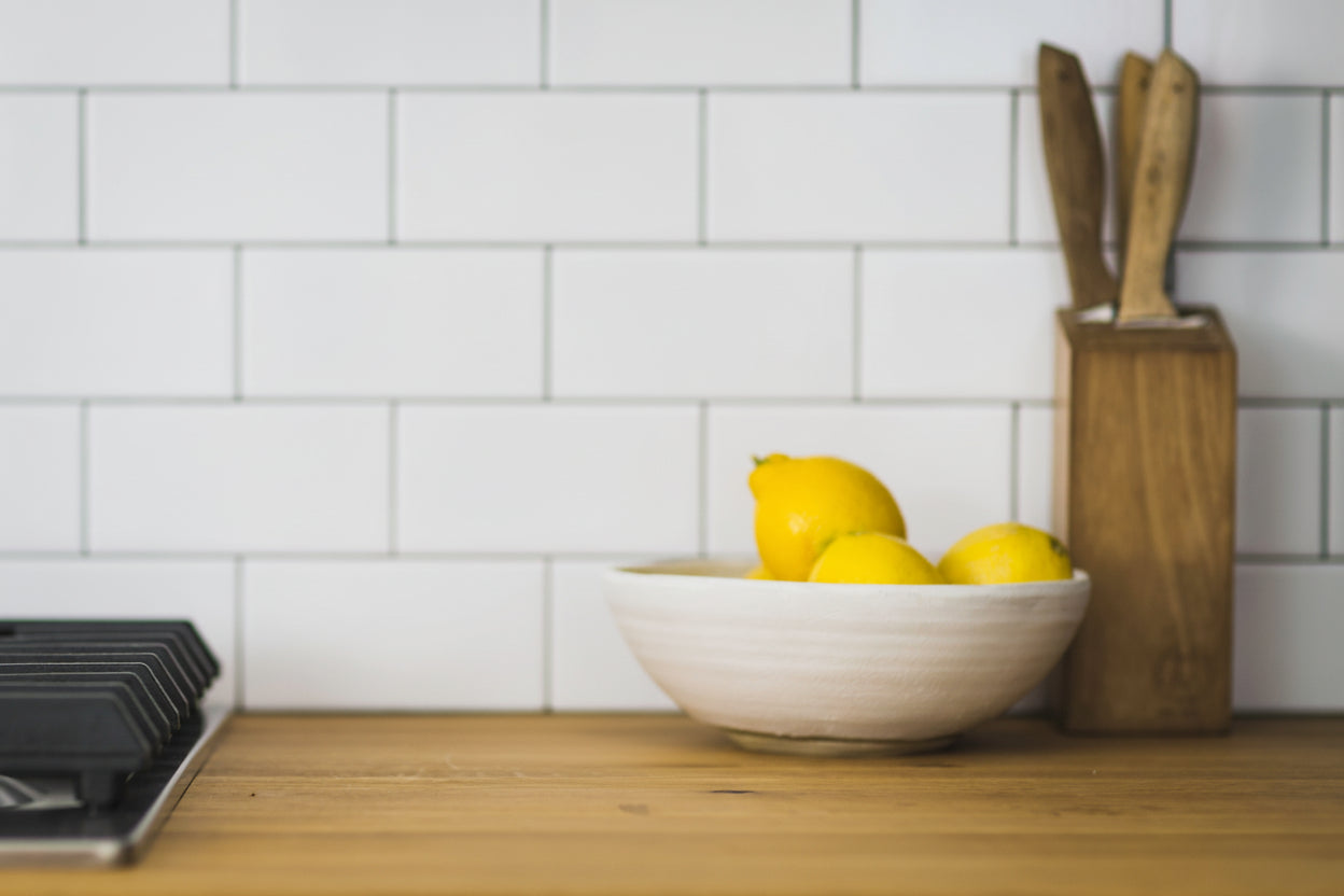 Bowl of fresh lemons on a kitchen counter with white tile backsplash